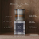 A premium 12 oz candle shown with its branded box on a wooden surface against a warm brown background. The candle has a plaid pattern in brown, beige, and black, with a lit wick.