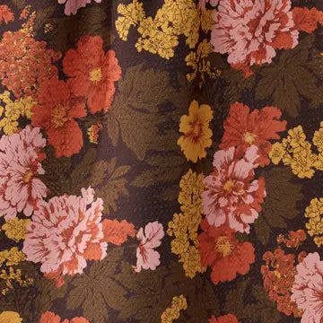 A close-up of a floral fabric pattern featuring large pink and orange flowers, yellow flower clusters, and dark olive green leaves on a dark brown background.