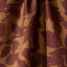 A close-up of draped fabric with a waffle-weave texture, featuring a dark burgundy leaf pattern over a warm tan background.