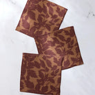 Three square woven coasters with a brown and tan leaf pattern, arranged diagonally on a white marble surface.