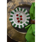 Decorative plate with cherry design on a green and white striped border, placed on a textured surface with a green napkin.