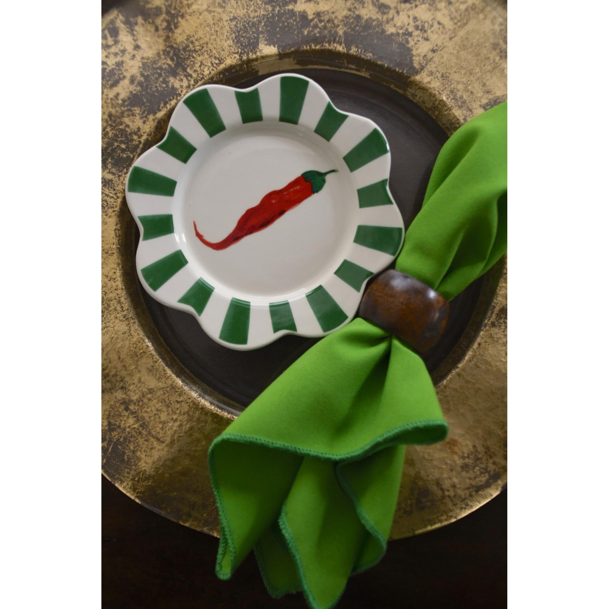 Decorative plate with a red chili pepper design on a green rim, placed on a textured surface with a green napkin.