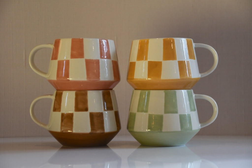 Two sets of checkered ceramic mugs stacked on a reflective surface with a neutral background