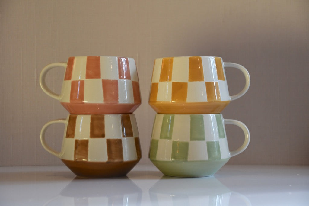 Set of four checkered ceramic mugs stacked on a reflective surface with a neutral background